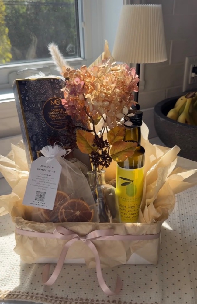 A styled gift basket with olive oil, dried flowers and a pink ribbon